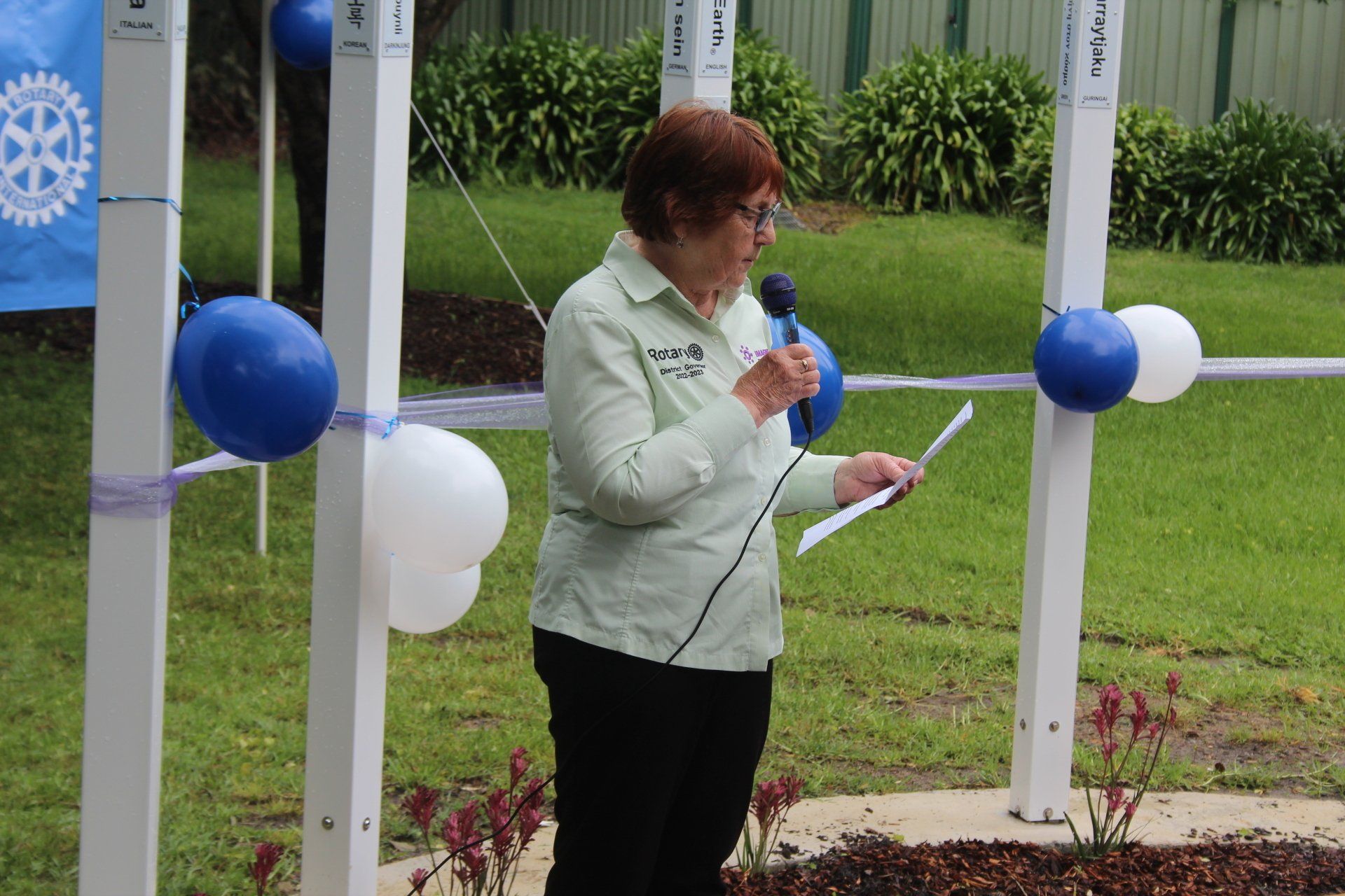 A woman is speaking into a microphone while holding a piece of paper