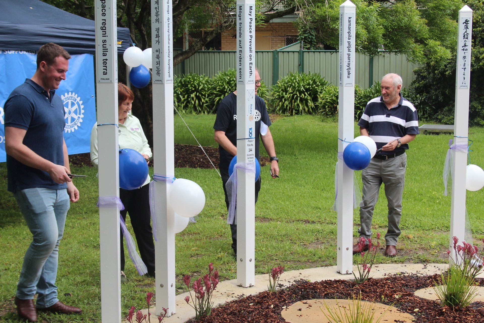 A group of people are standing around a row of white poles with balloons on them.