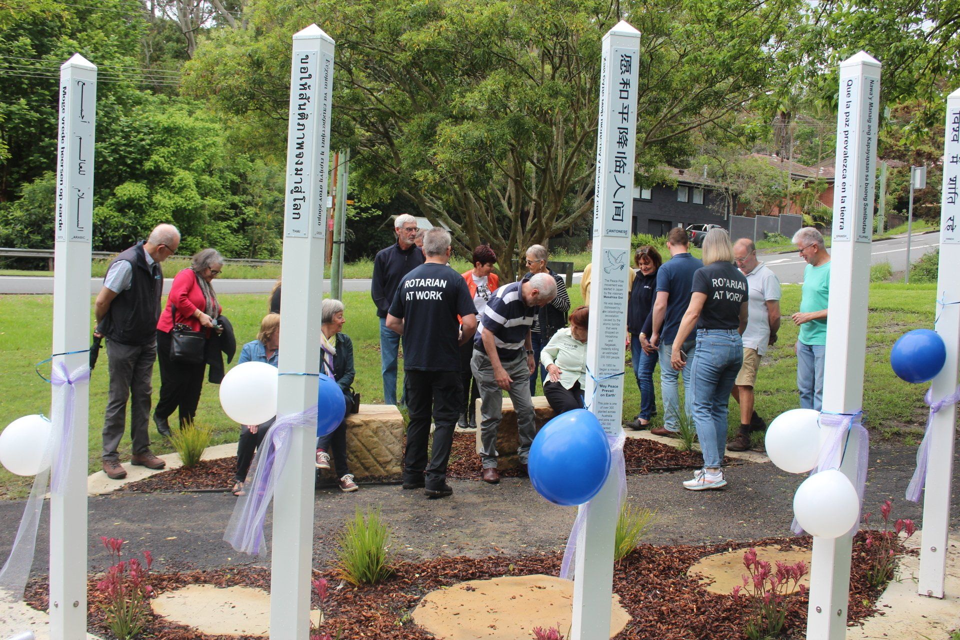 A group of people are standing around a row of white poles with blue and white balloons.