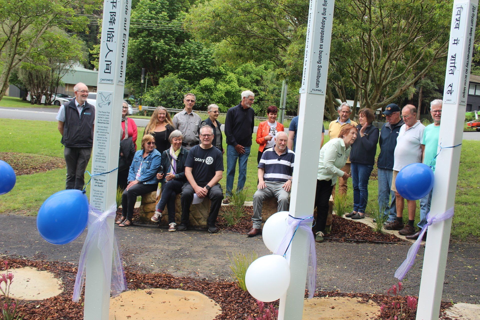 A group of people are standing around a row of white poles with blue and white balloons.