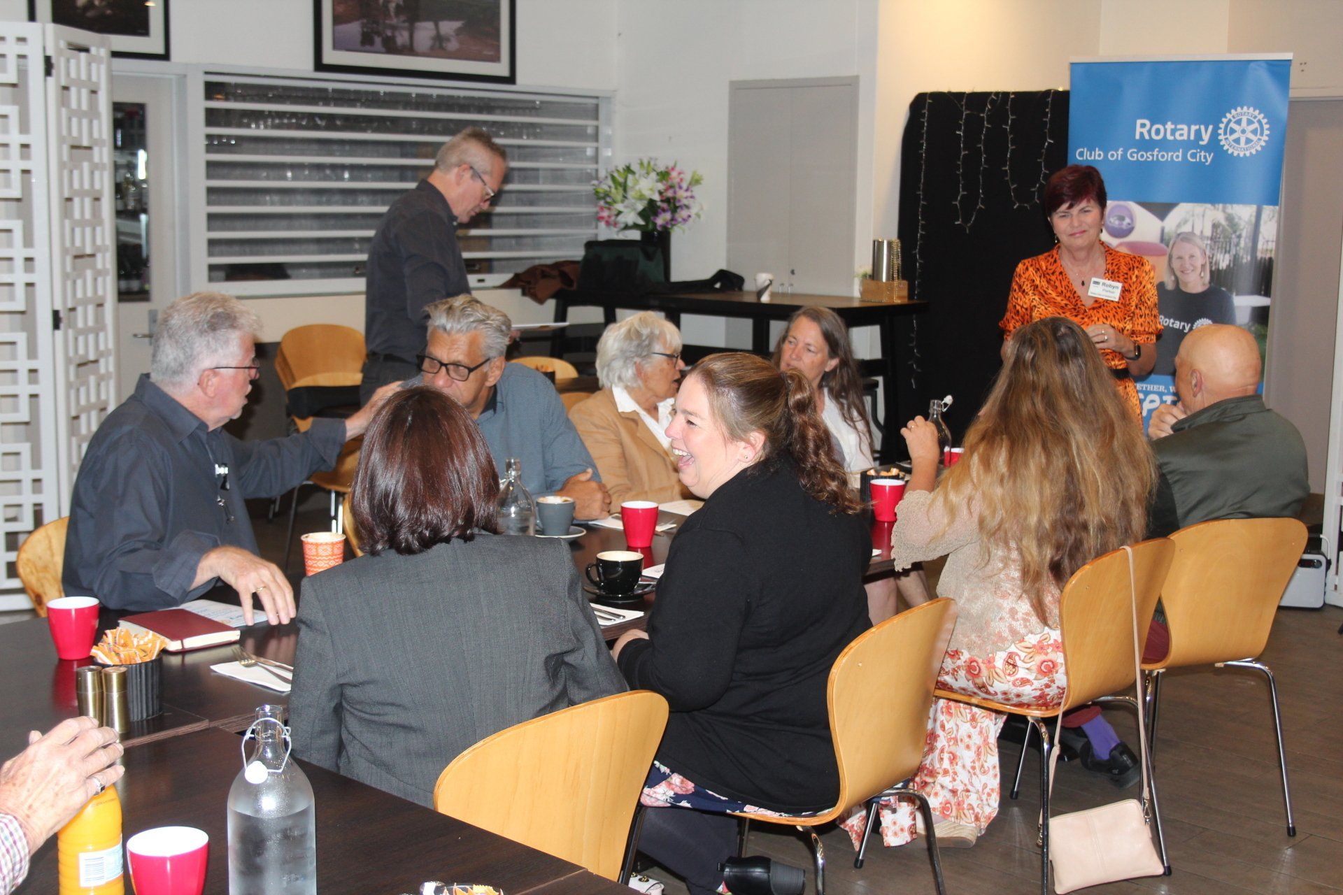 A group of people are sitting around a table with a rotary sign in the background