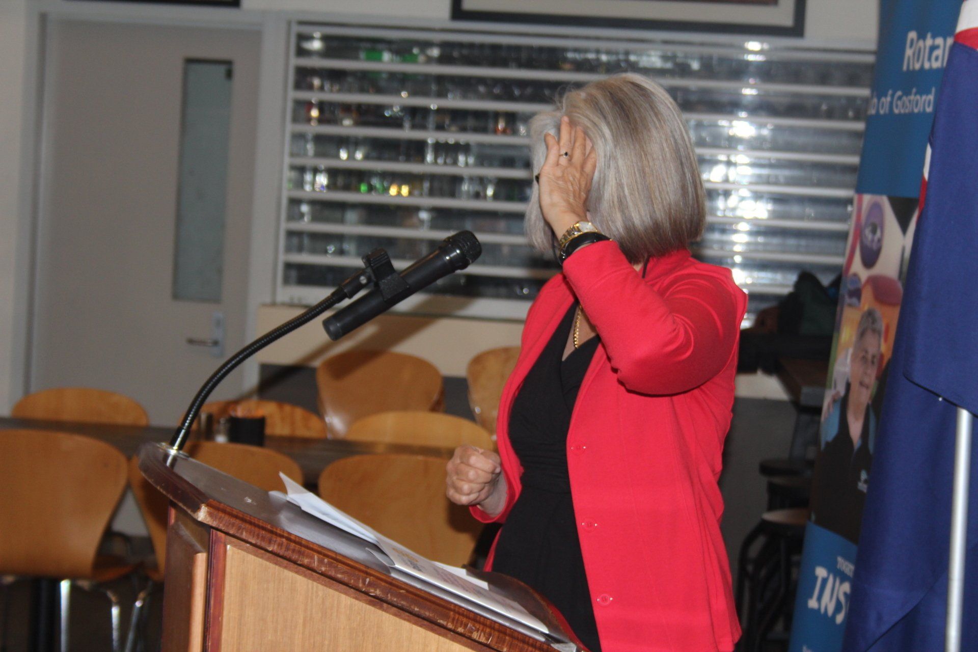 A woman in a red jacket is speaking into a microphone