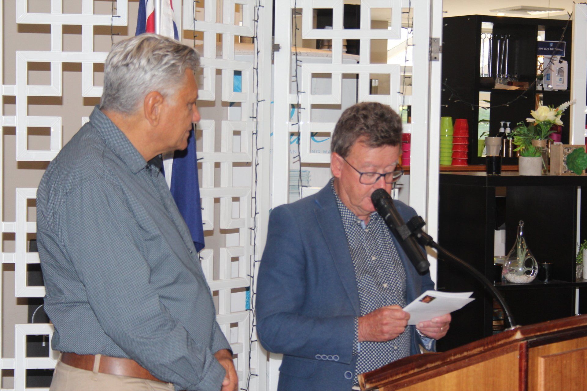 Two men are standing in front of a podium and one is reading a piece of paper