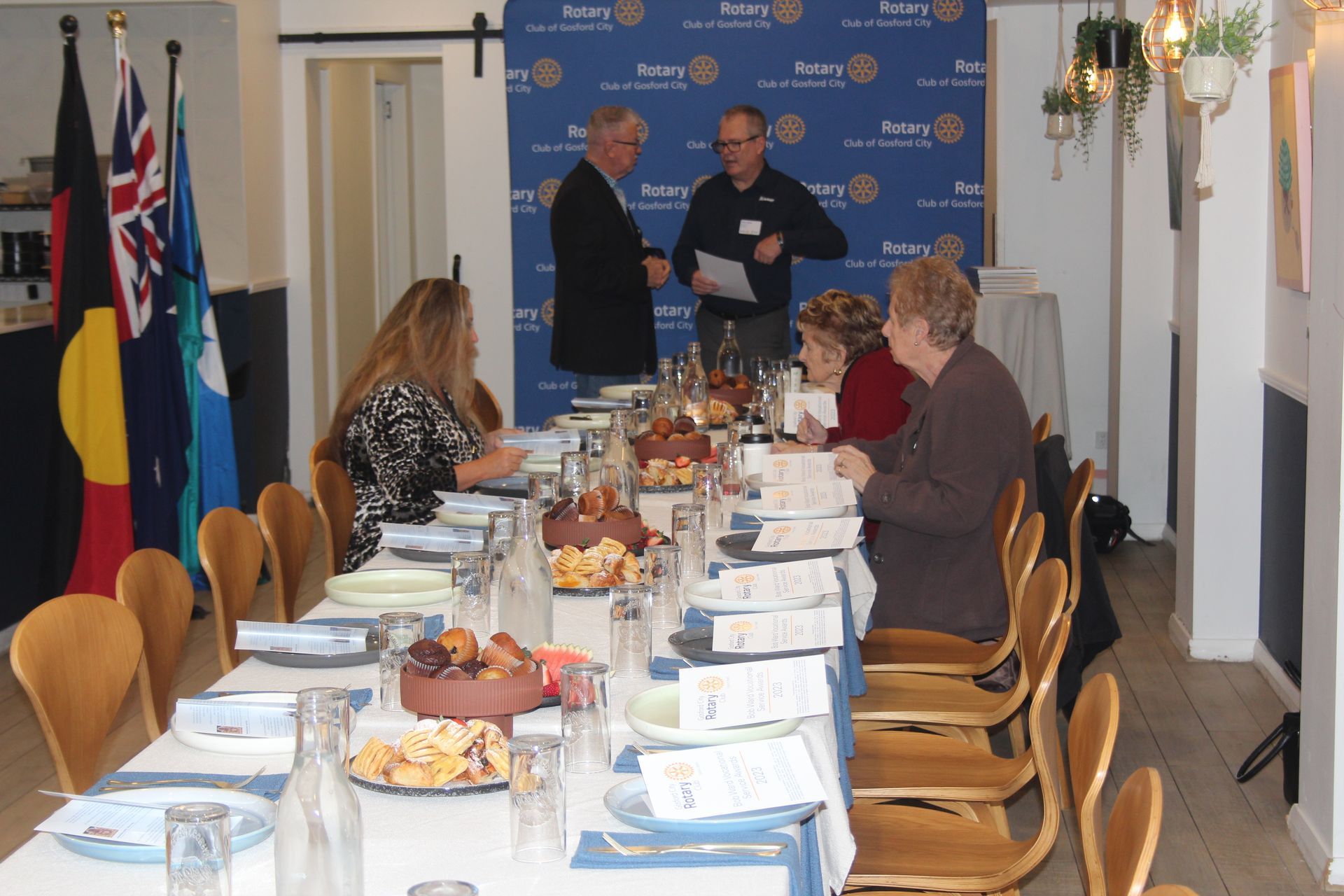 A group of people are sitting at a long table in front of a wall that says rotary