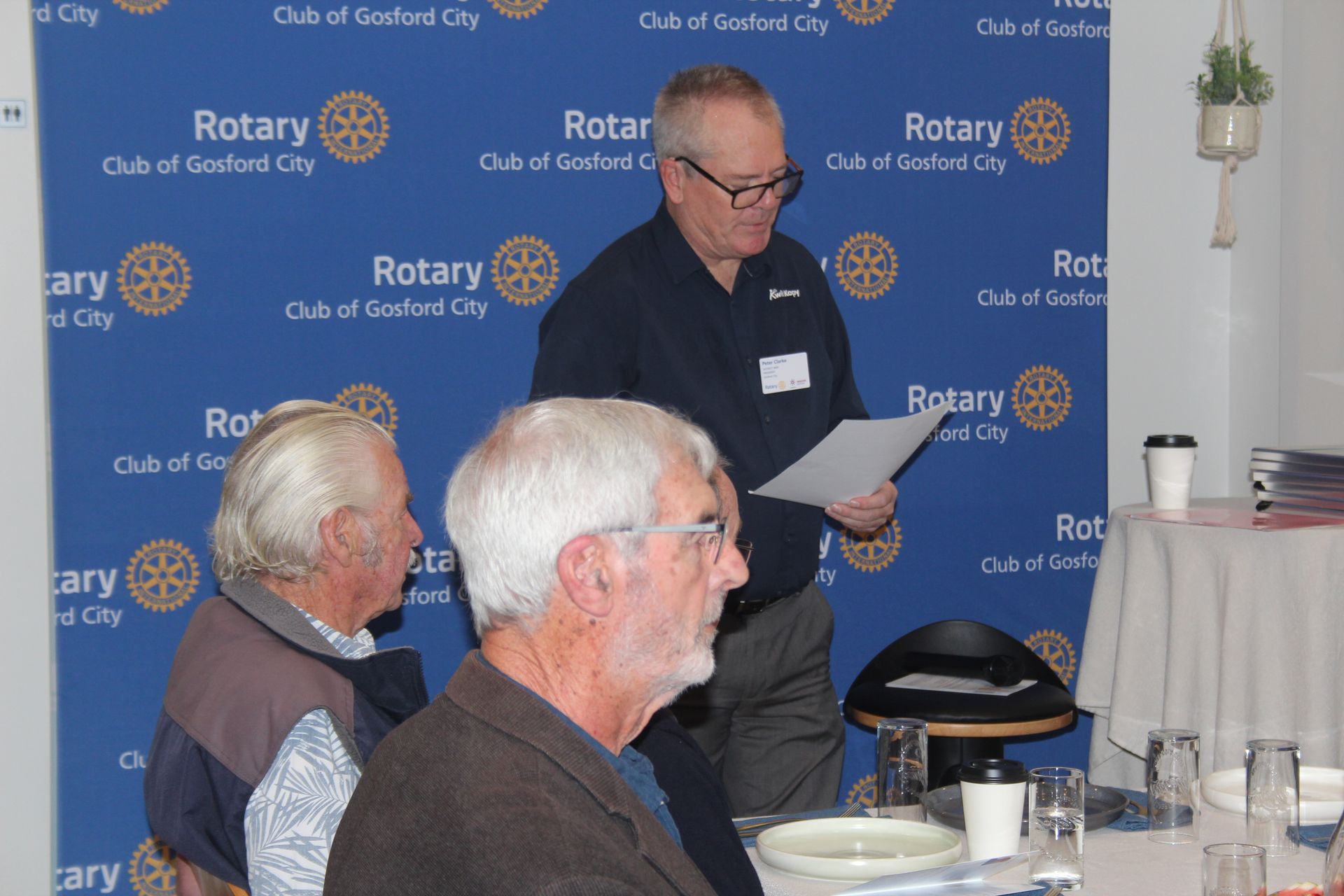 A group of men are sitting at a table in front of a wall that says rotary