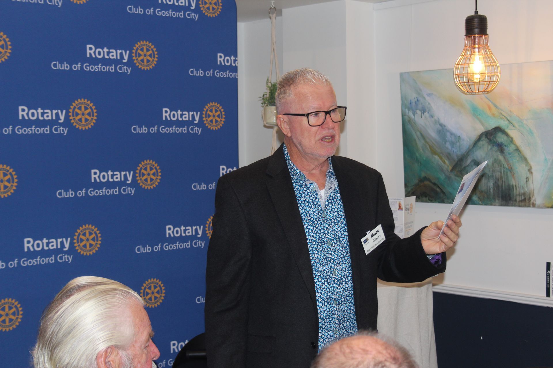 A man in a suit is holding a piece of paper and talking to a group of people.