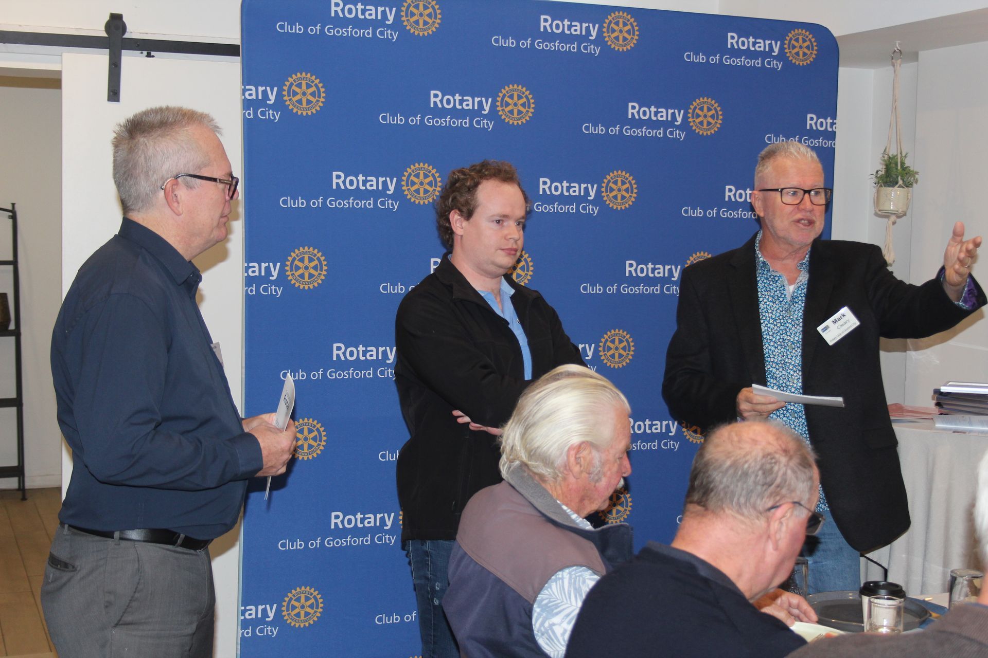 A group of men are standing in front of a wall that says rotary