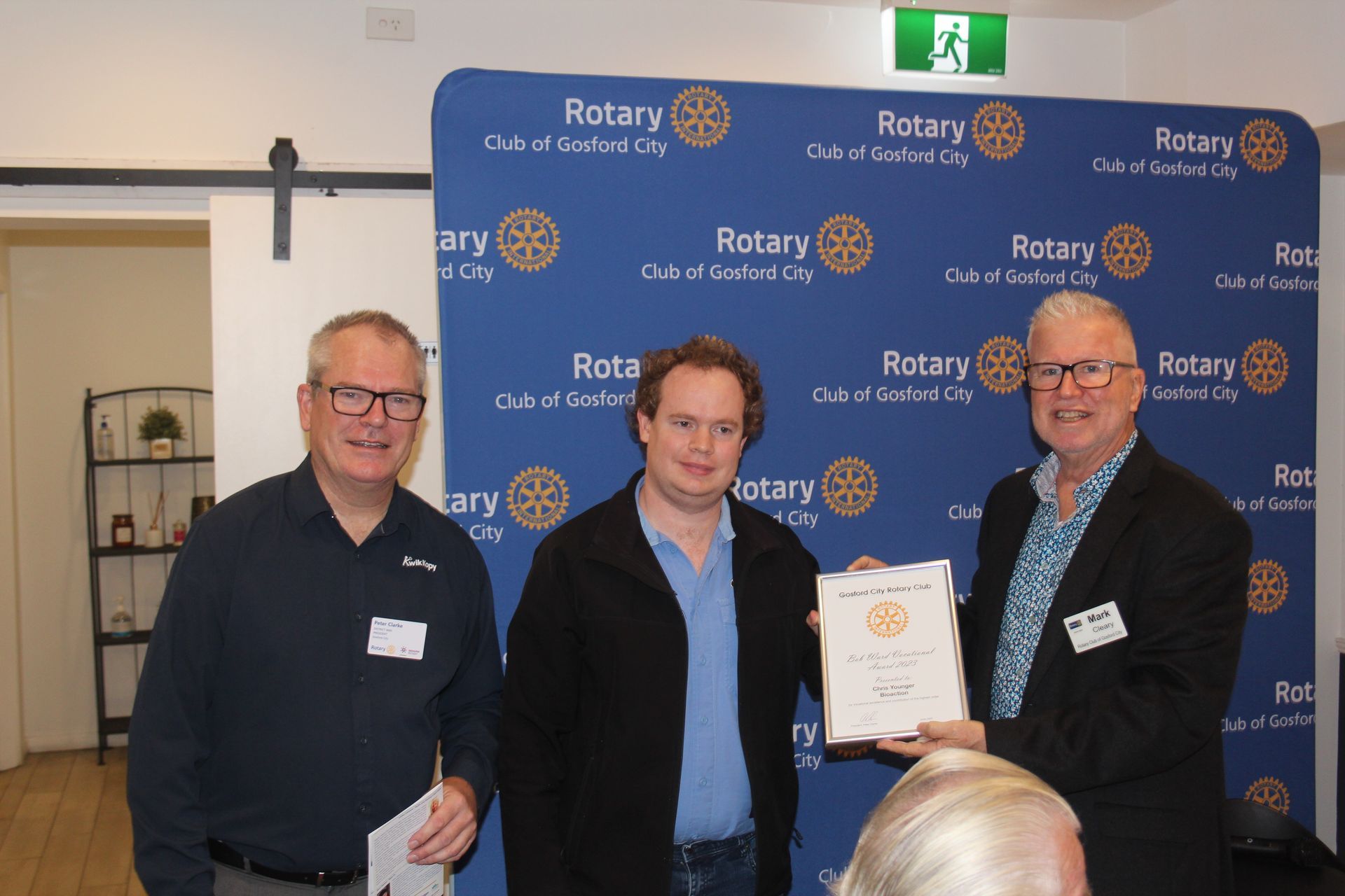 Three men are standing next to each other in front of a wall that says rotary.