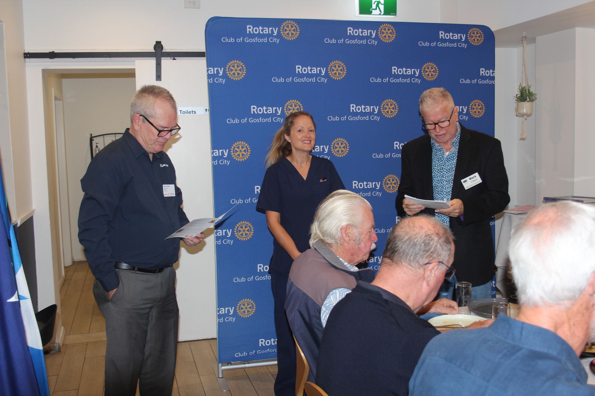A group of people standing in front of a wall that says rotary