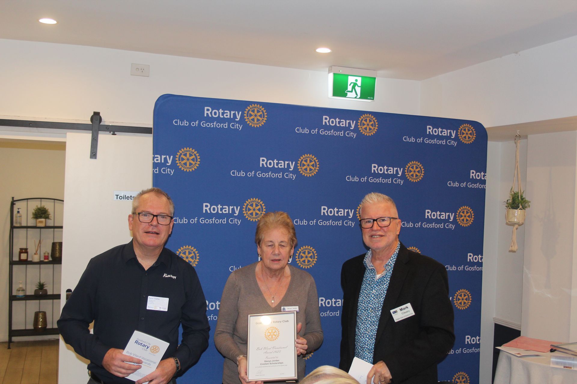 Three people are standing in front of a wall that says rotary