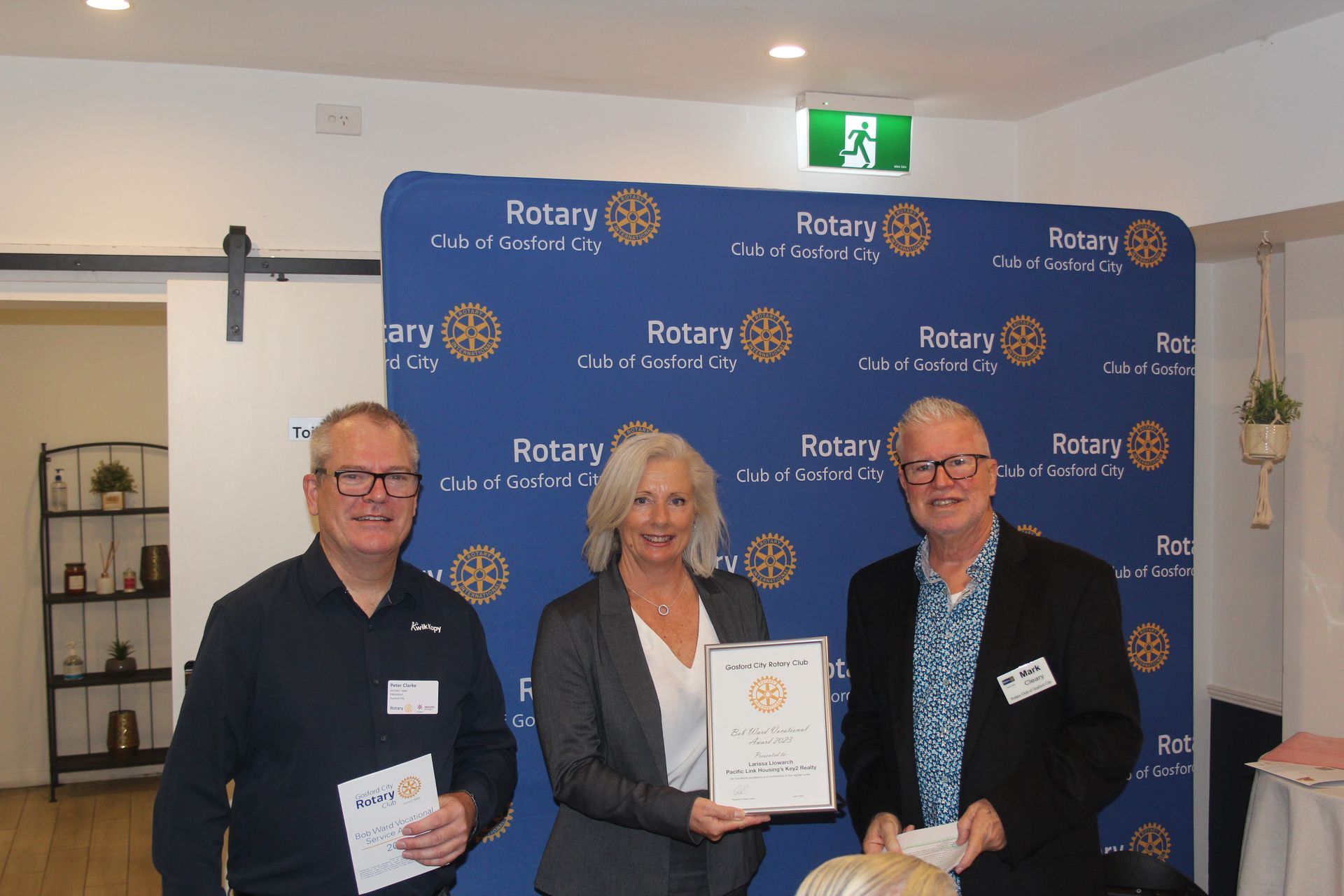 Three people are standing next to each other in front of a wall that says rotary.