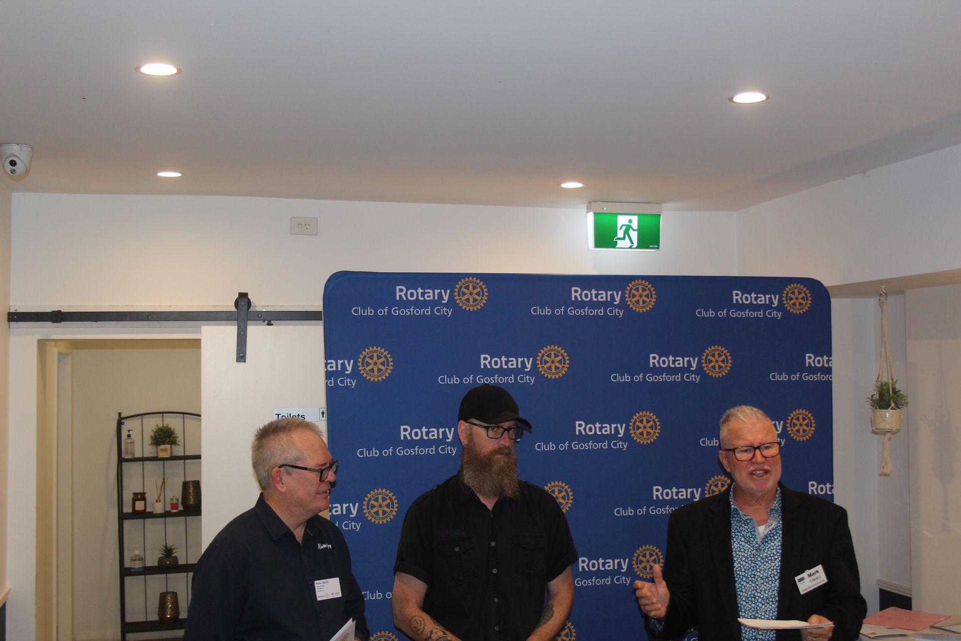 Three men are standing in front of a blue backdrop that says rotary.