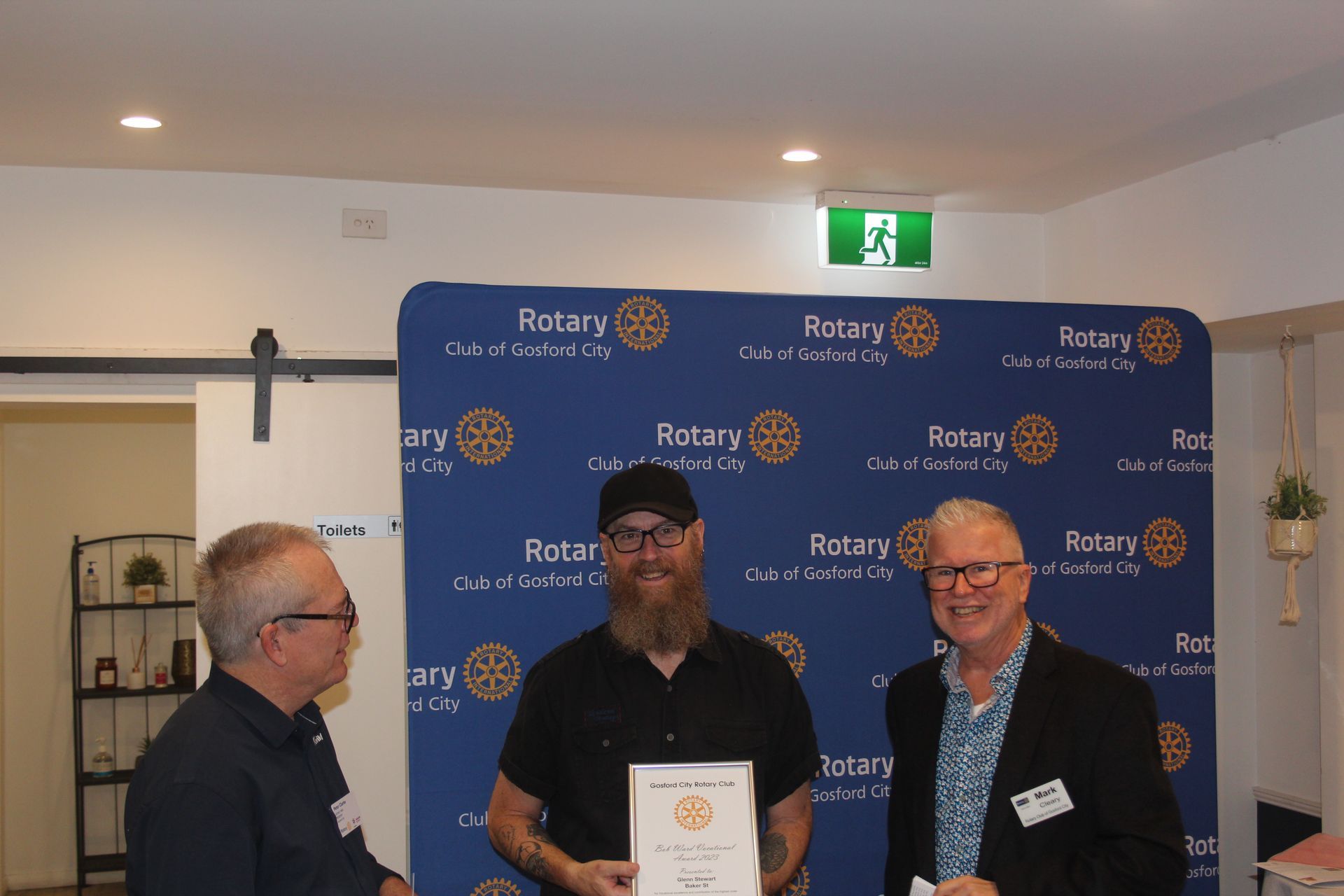 Three men are standing in front of a blue backdrop holding a certificate.