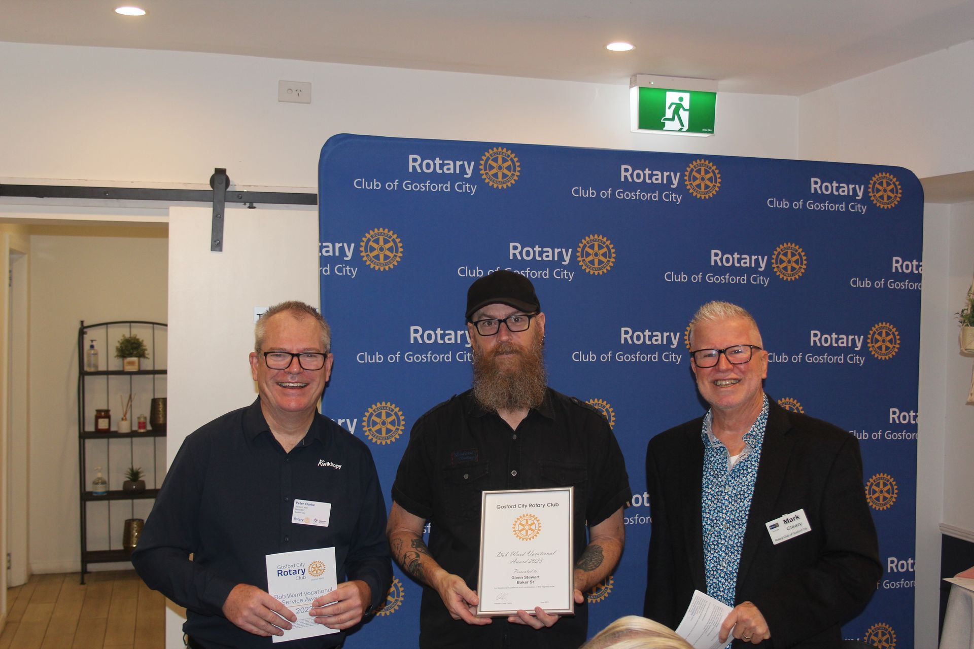 Three men are standing next to each other in front of a blue backdrop that says rotary.