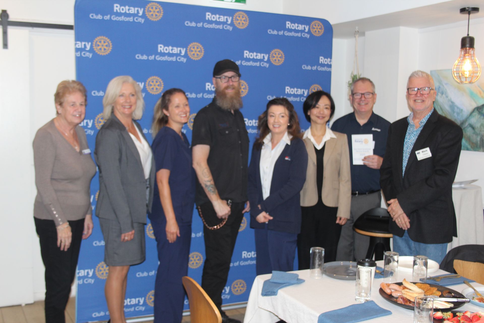A group of people are posing for a picture in front of a wall that says rotary