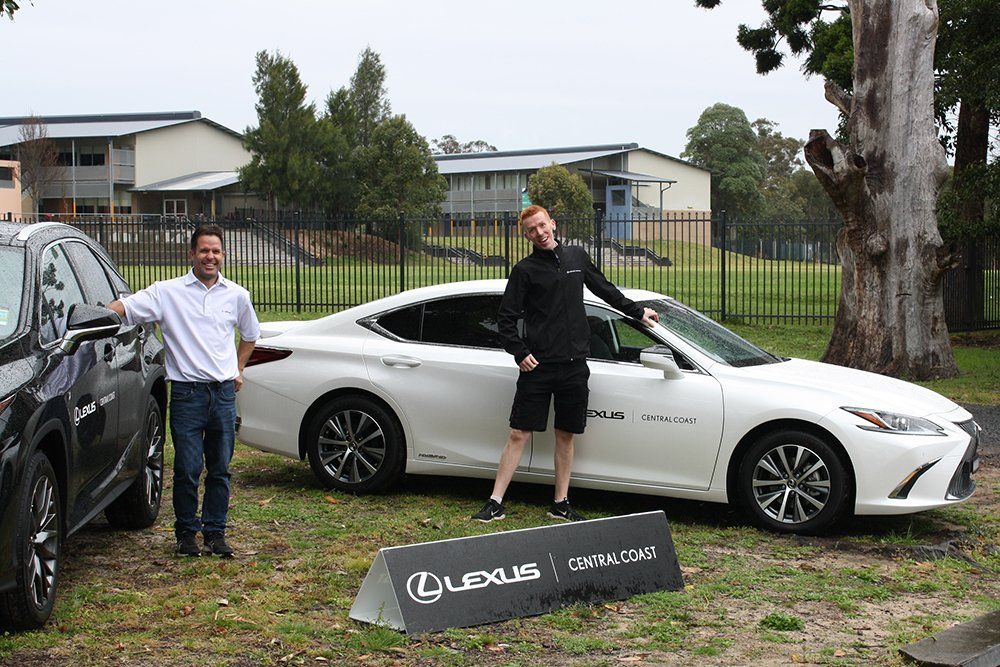Two men are standing next to a white lexus car.