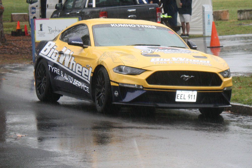 A yellow mustang is driving down a wet road