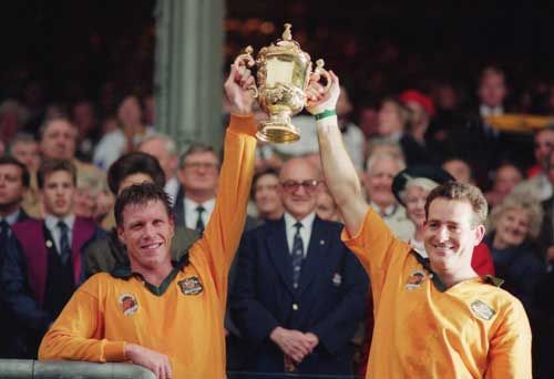 Two men are holding a trophy in their hands in front of a crowd.