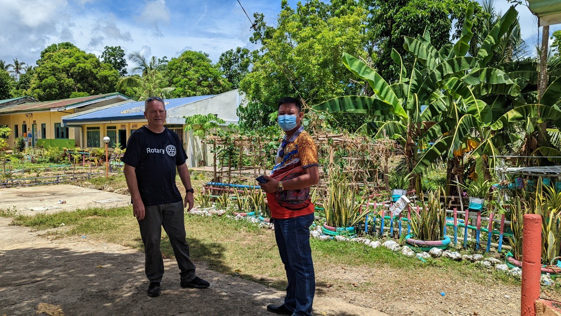 Two men wearing face masks are standing in front of a house.