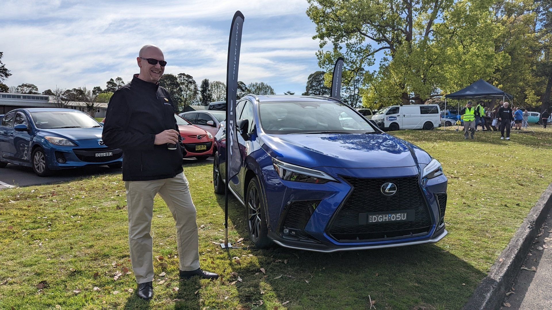 A man is standing in front of a blue lexus car.