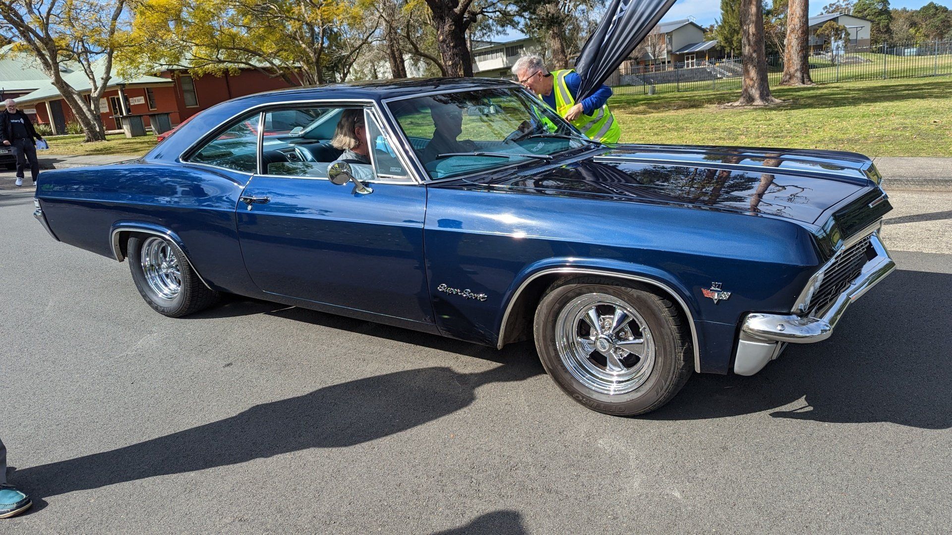 A man is standing next to a blue car on the side of the road.