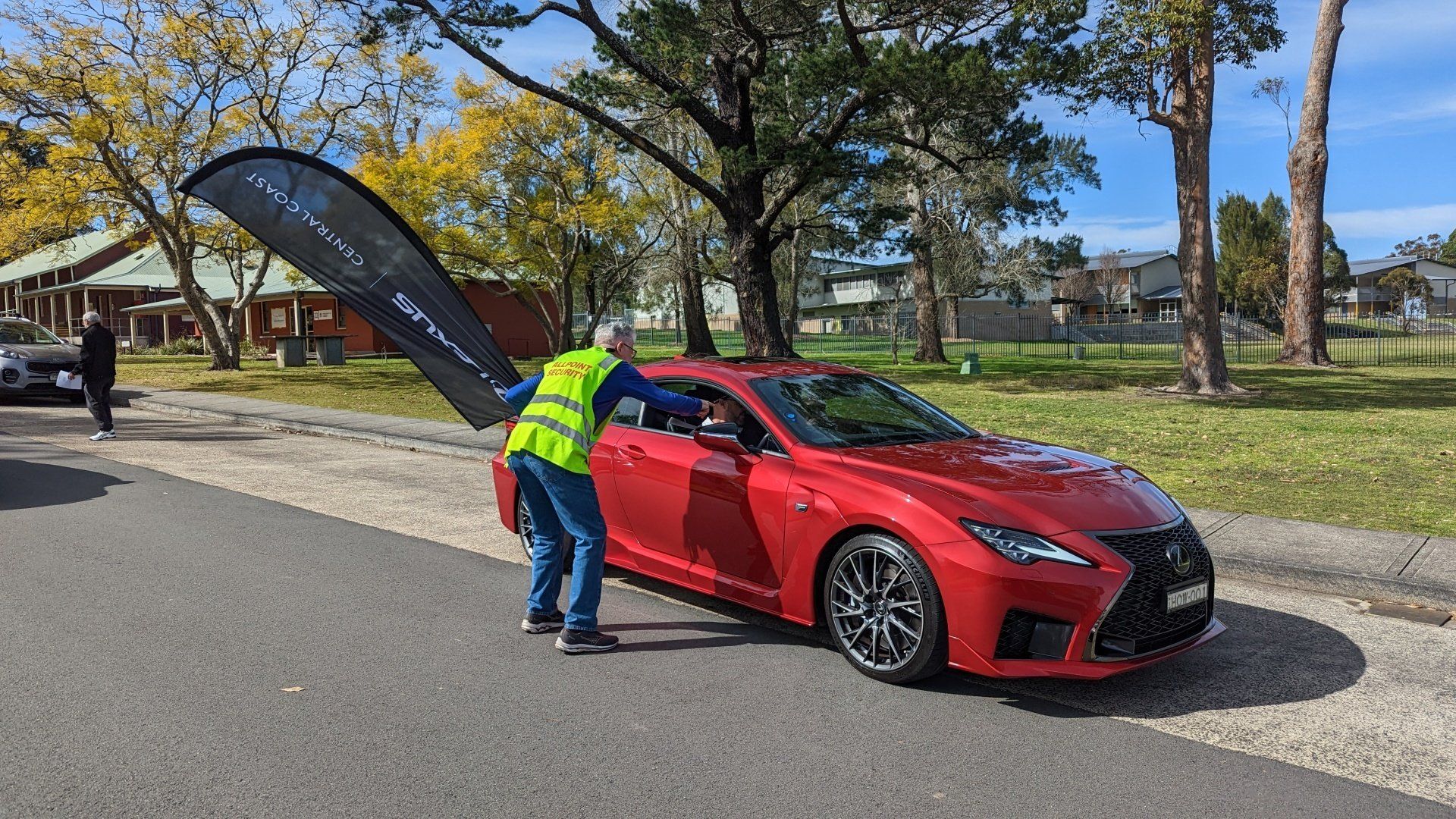 A man in a yellow vest is standing next to a red car.