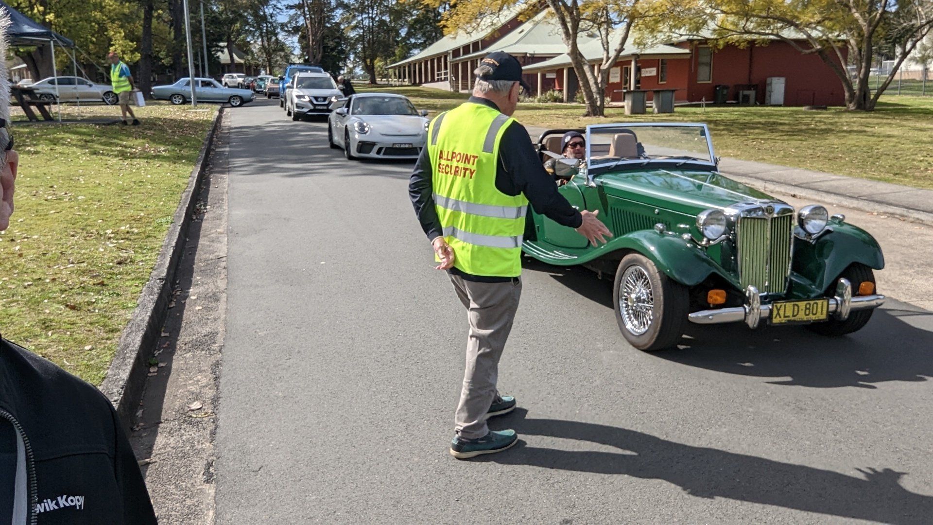 A man in a yellow vest is standing next to a green car.