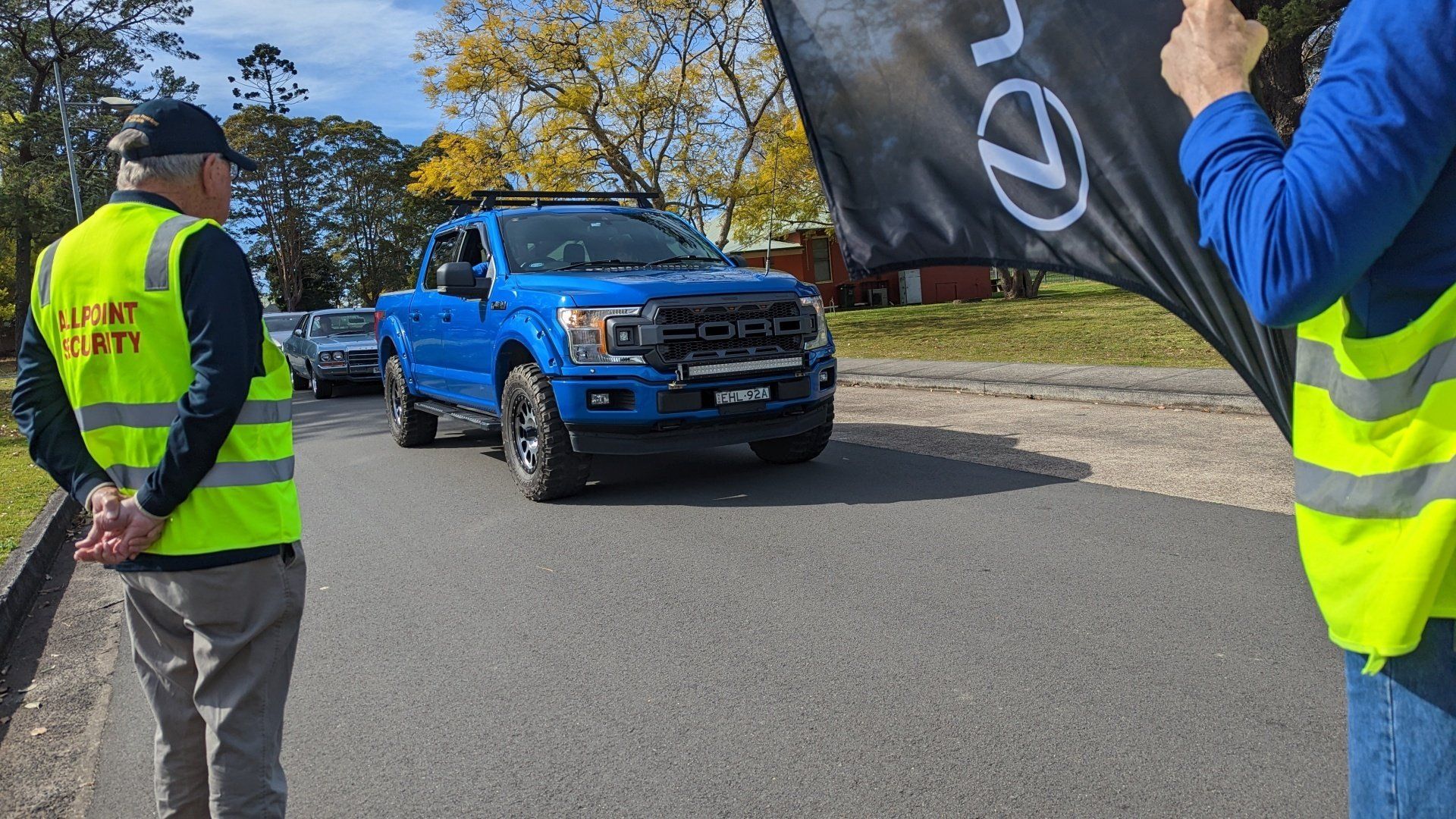 A man in a yellow vest is standing next to a blue truck.