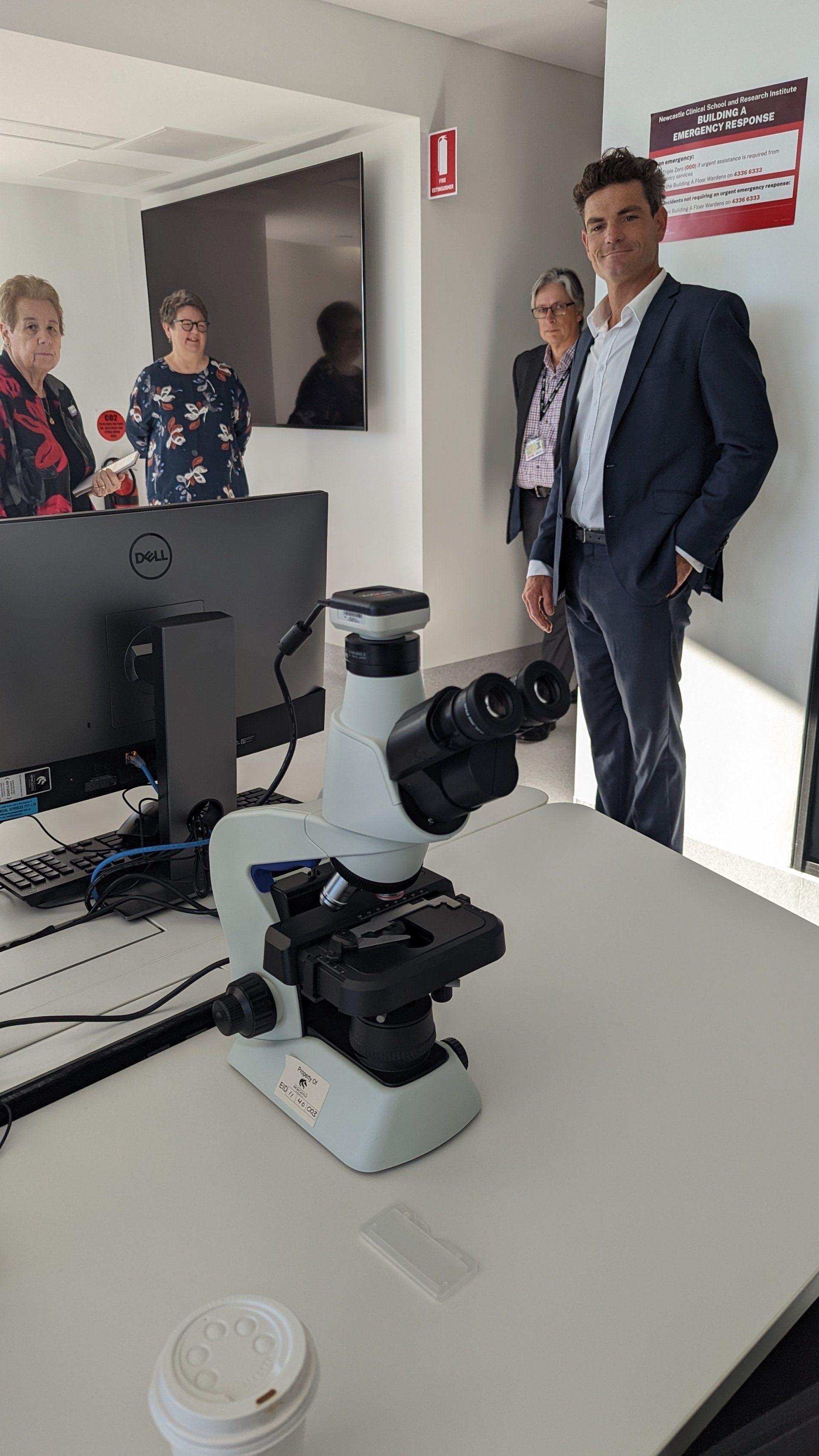 A group of people are standing around a microscope in a room.