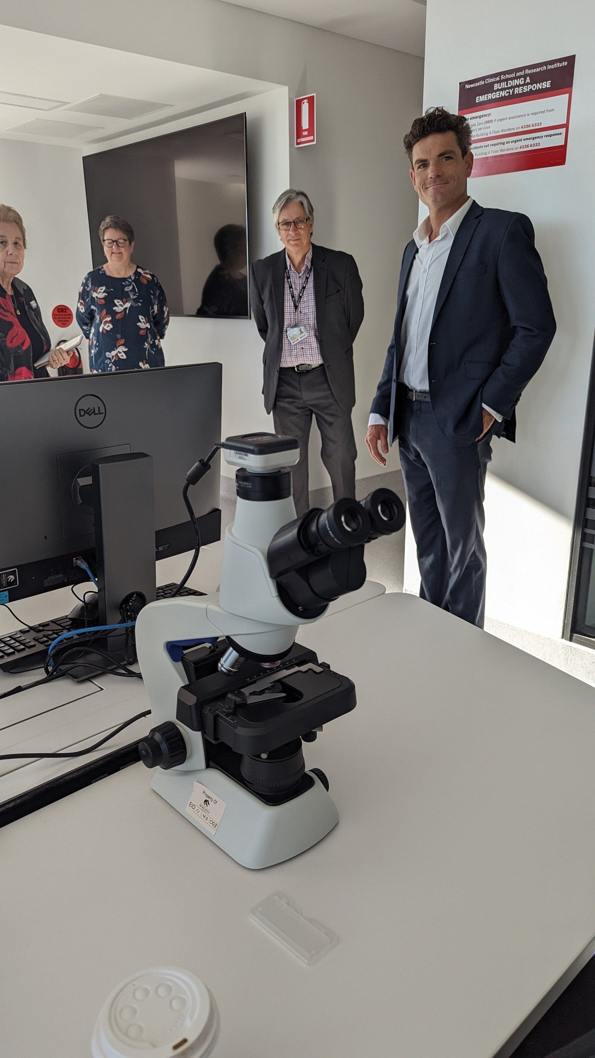 A group of people are standing around a microscope on a table.