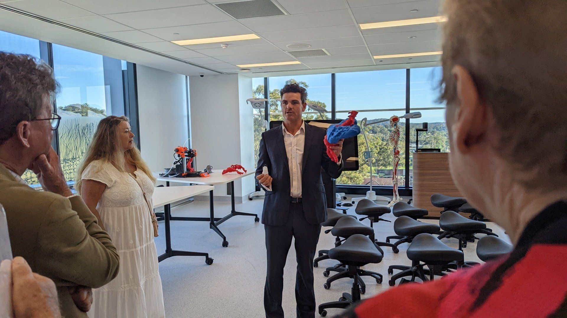 A man in a suit is standing in a room talking to a group of people.