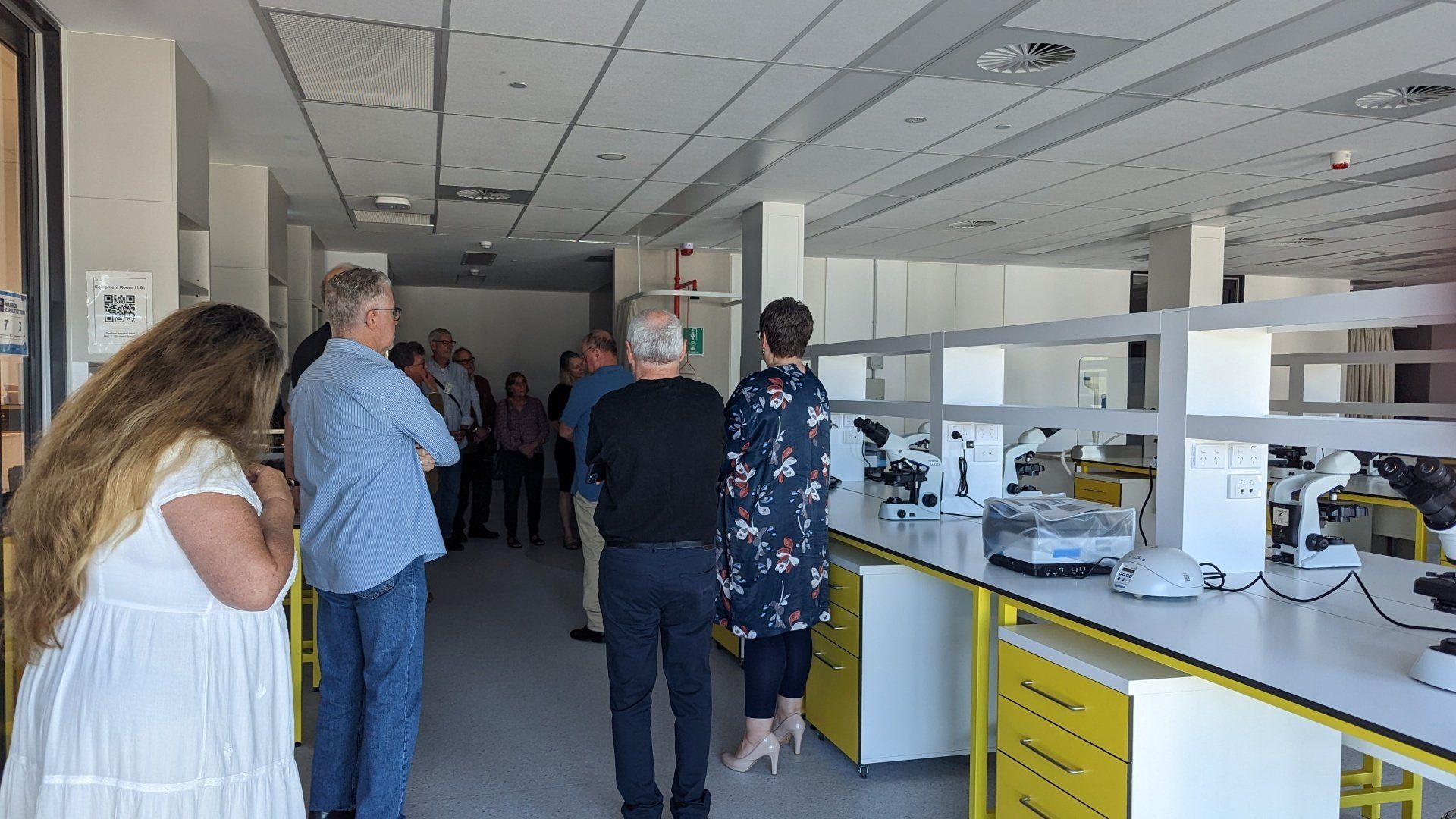 A group of people are standing in a lab looking at microscopes.