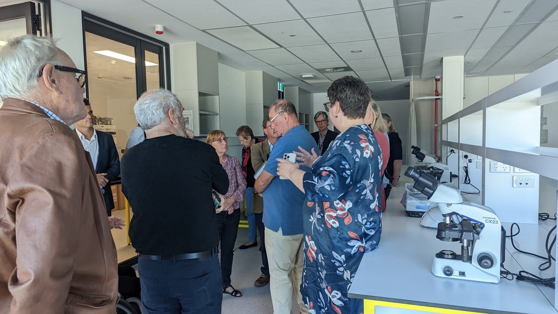 A group of people are standing in a room with microscopes.