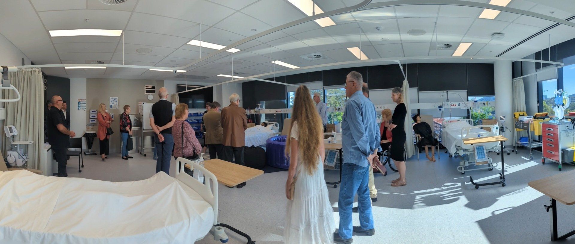 A group of people are standing in a hospital room looking at a hospital bed.