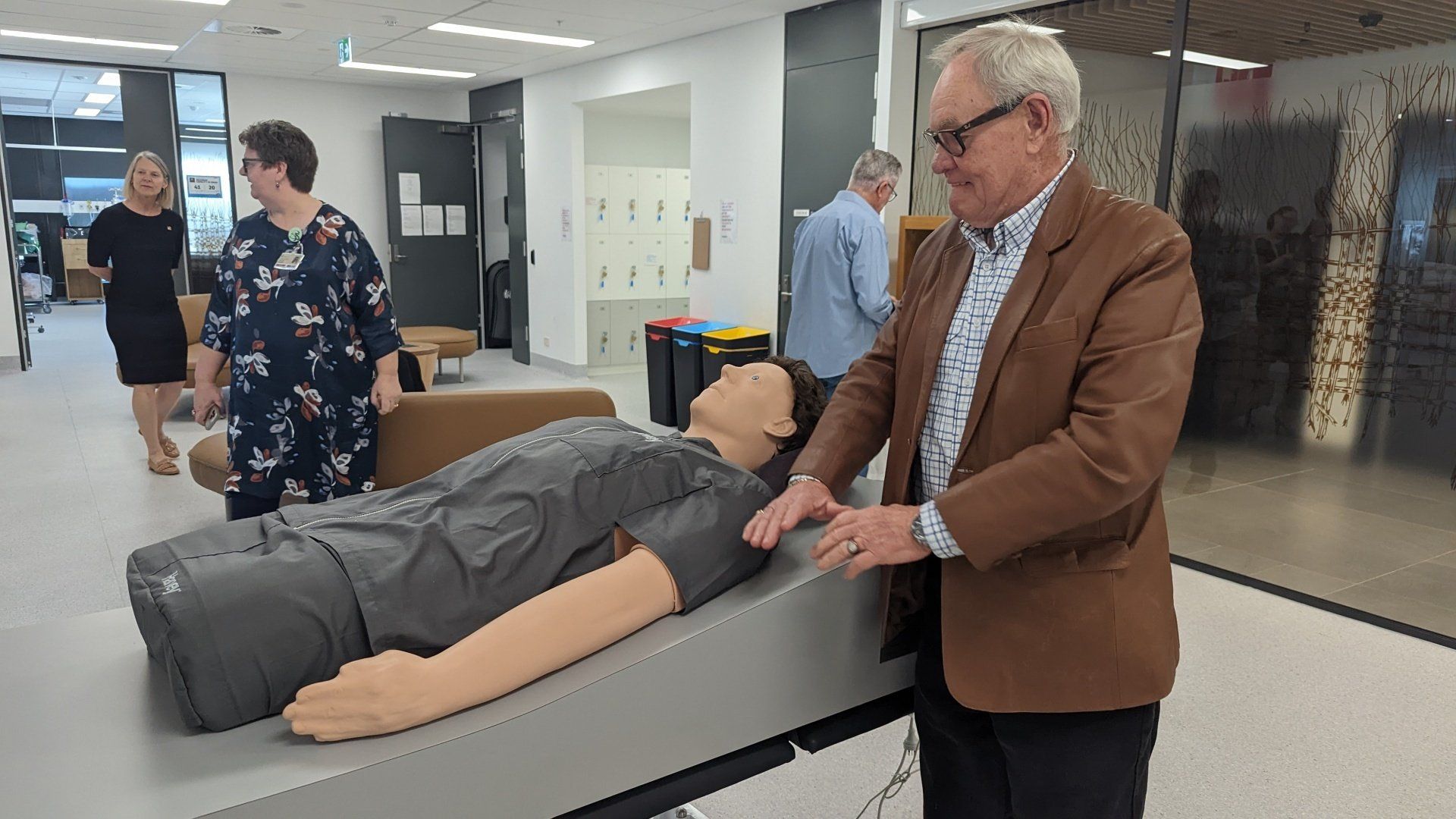A man in a brown jacket is standing next to a mannequin.