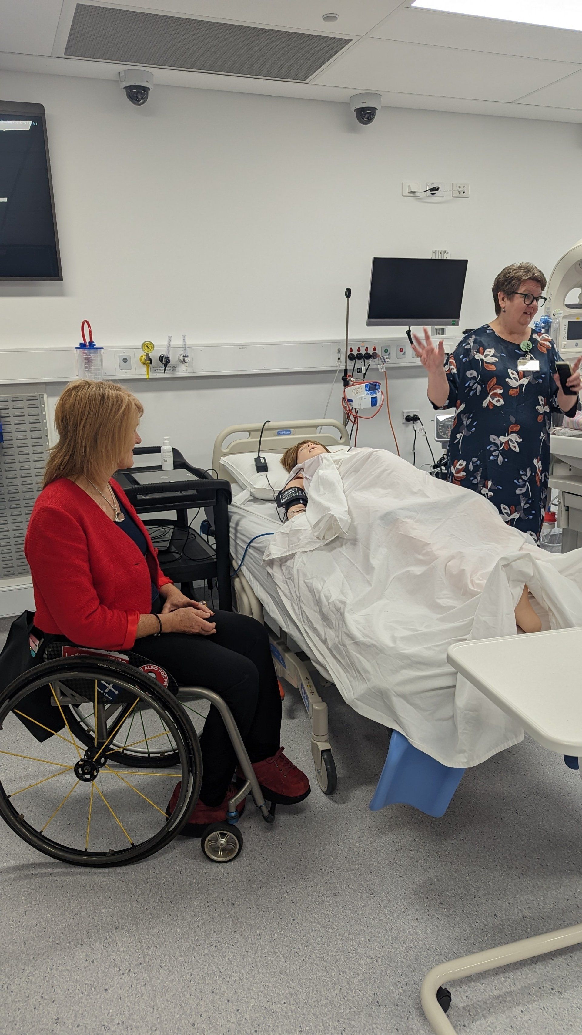 A woman in a wheelchair is sitting next to a woman in a hospital bed.