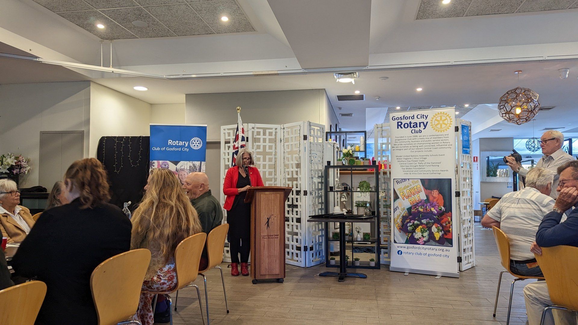 A woman is standing at a podium giving a speech to a group of people sitting in chairs.