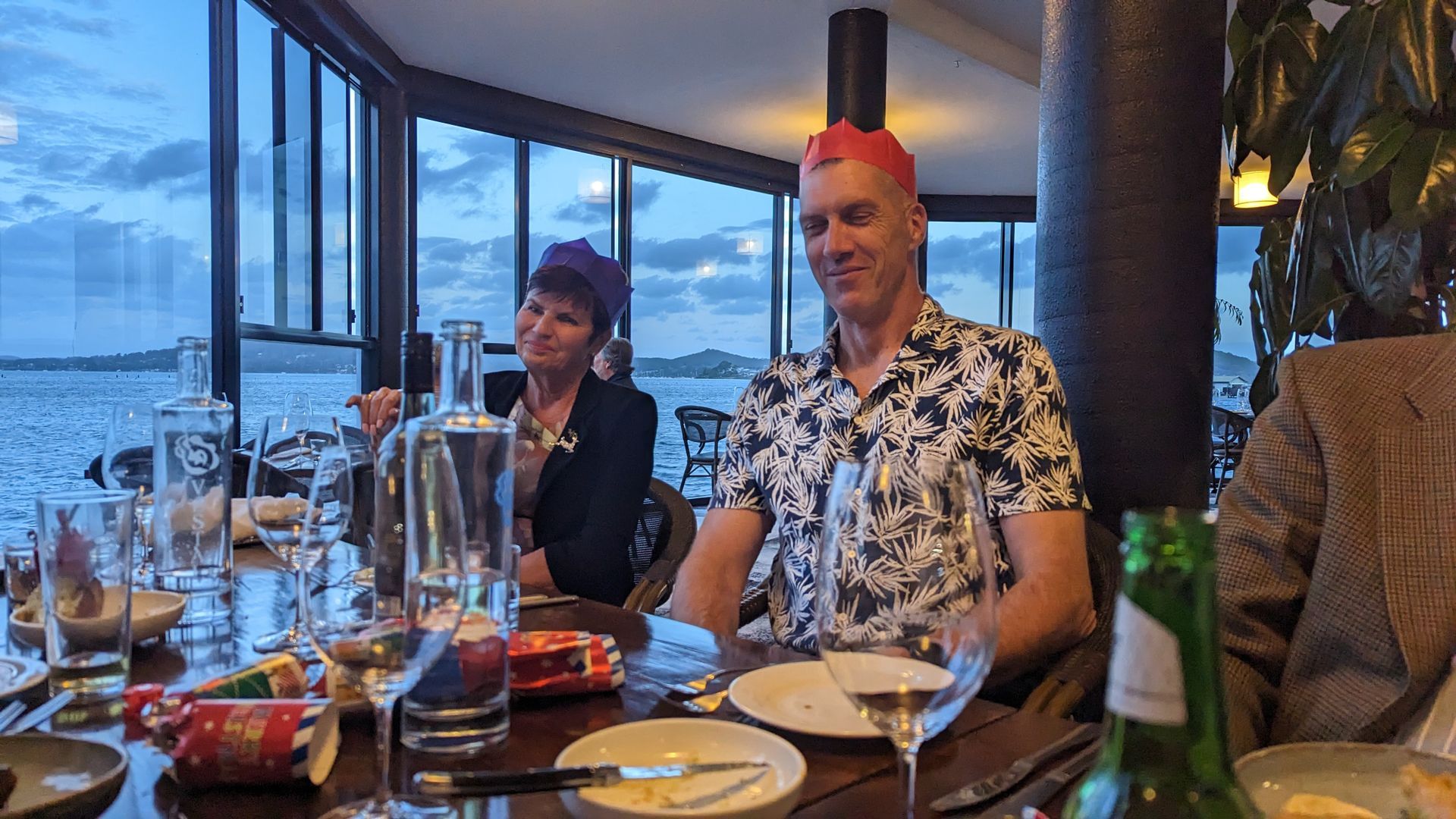 A man and a woman are sitting at a table with plates and glasses of wine.