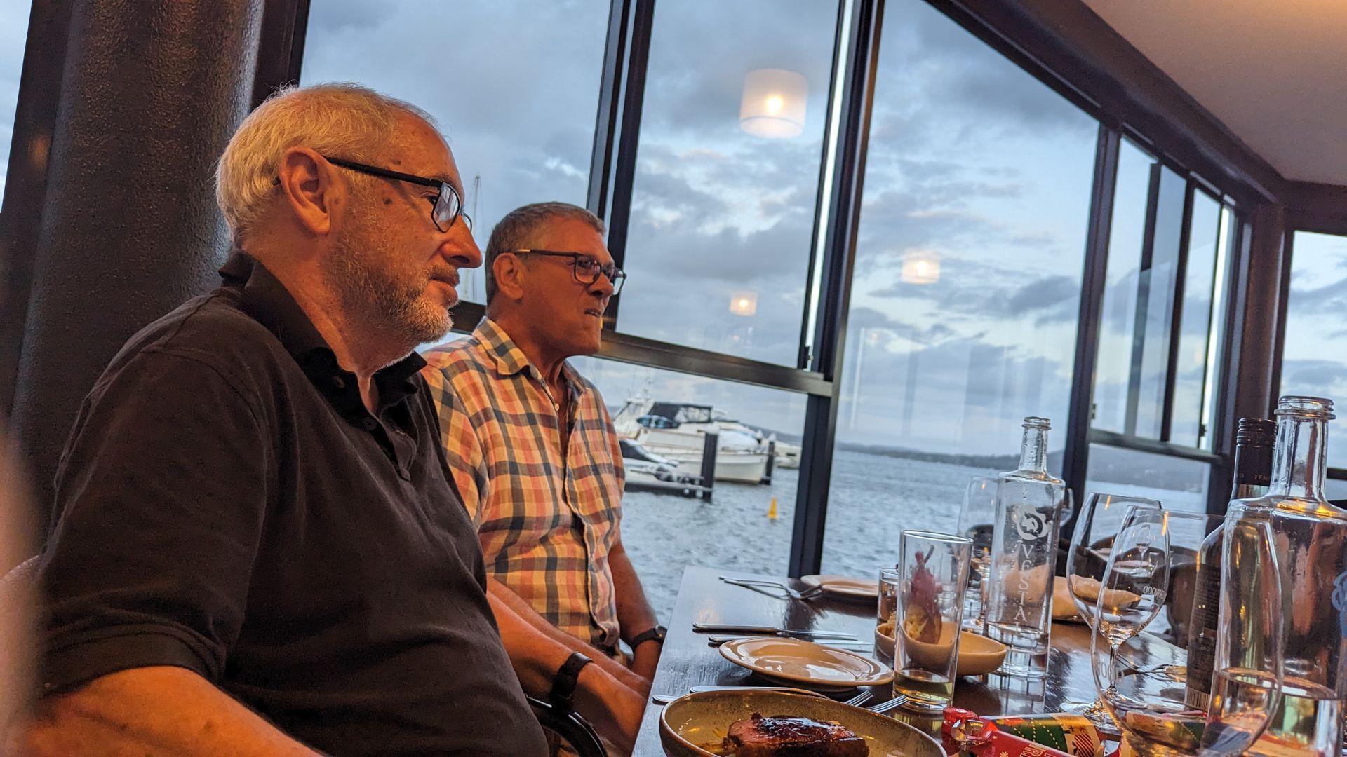 Two men are sitting at a table in front of a window.