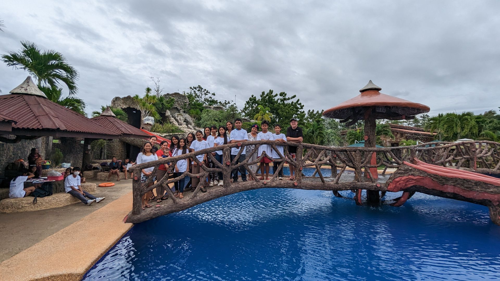 A group of people are standing on a bridge over a swimming pool.