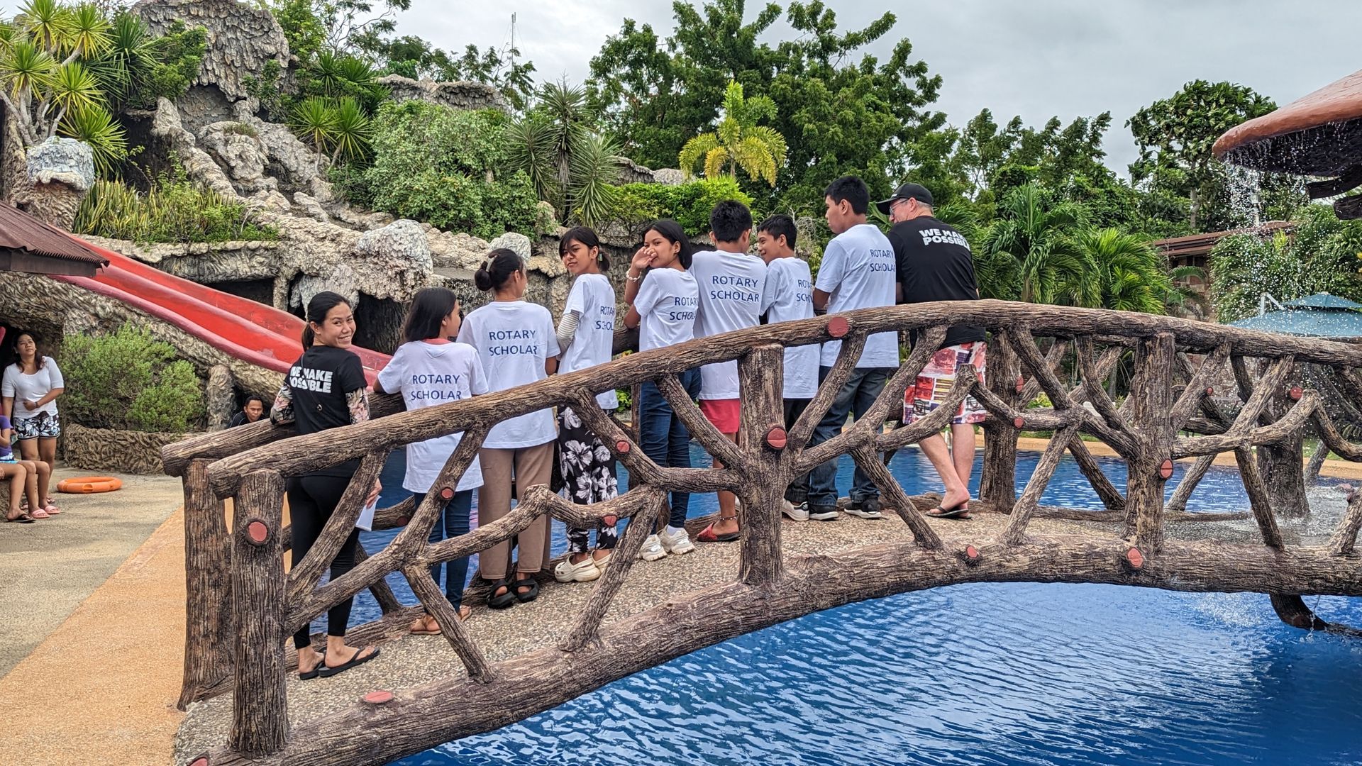 A group of people are standing on a wooden bridge over a pool.