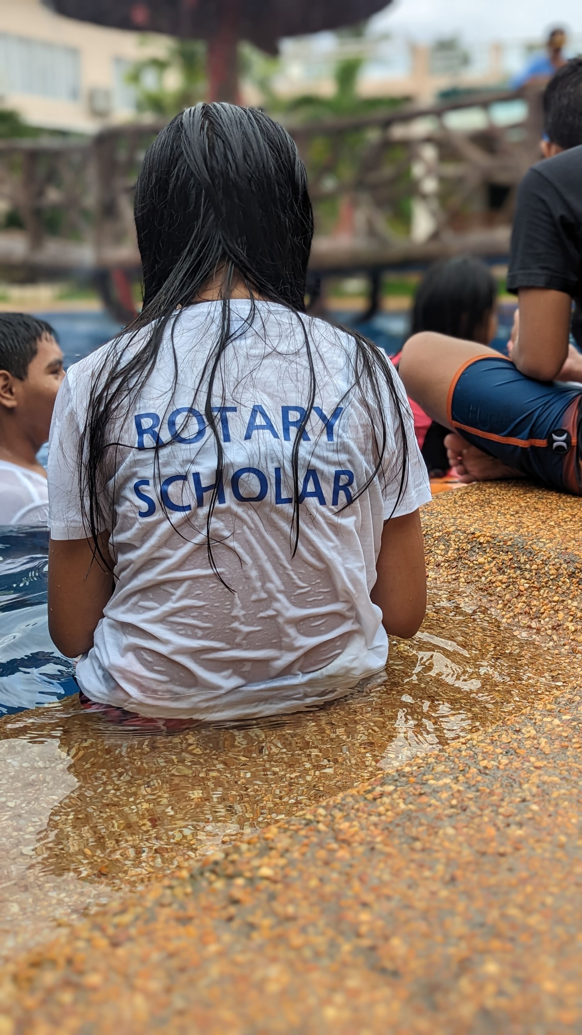 A girl in a wet shirt is sitting in the water.