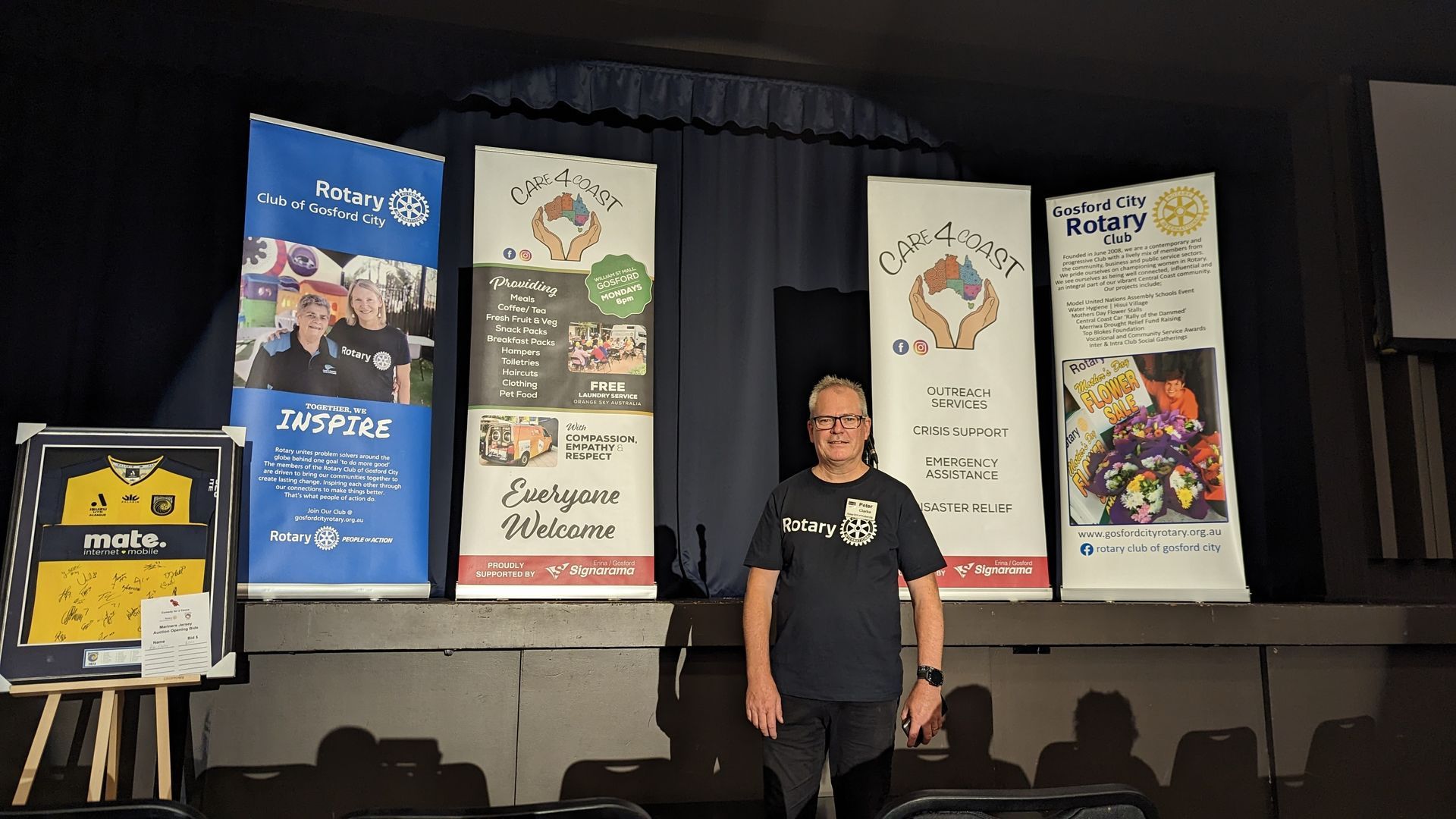 A man is standing in front of a stage with posters on it
