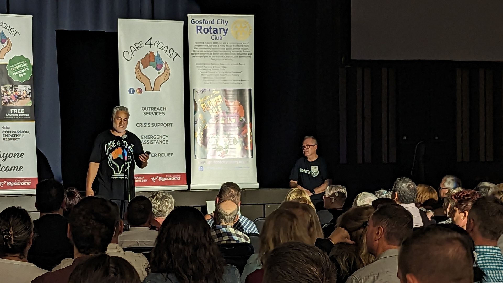 A group of people are sitting in front of a sign that says rotary
