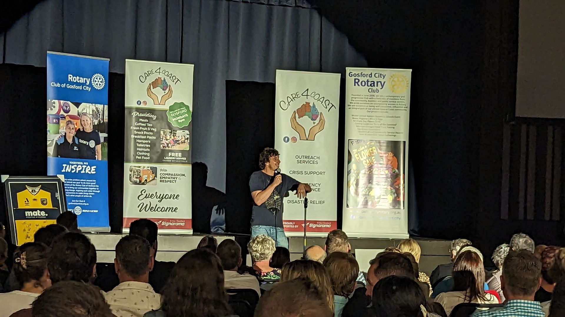 A man is standing on a stage with a microphone in front of a crowd of people.