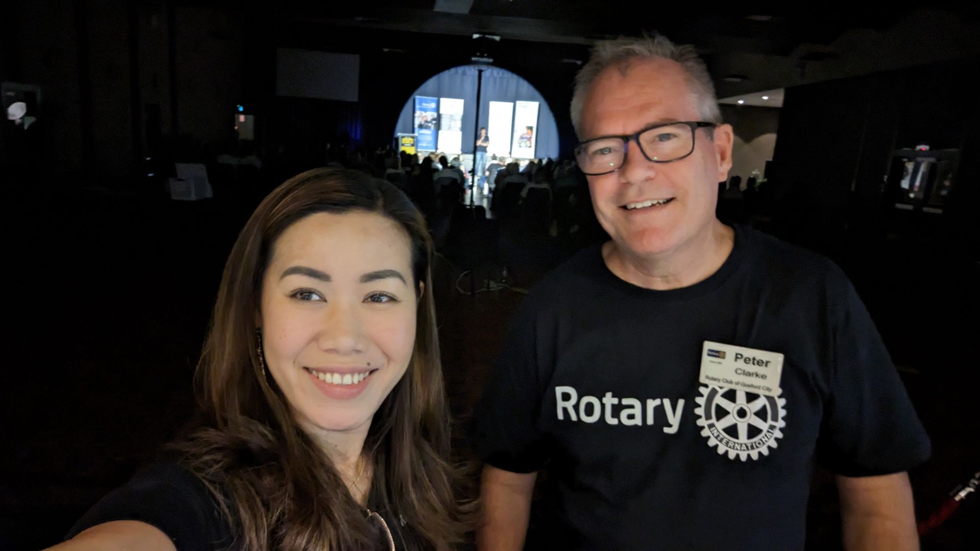 A man and a woman are posing for a picture together . the man is wearing a rotary shirt.