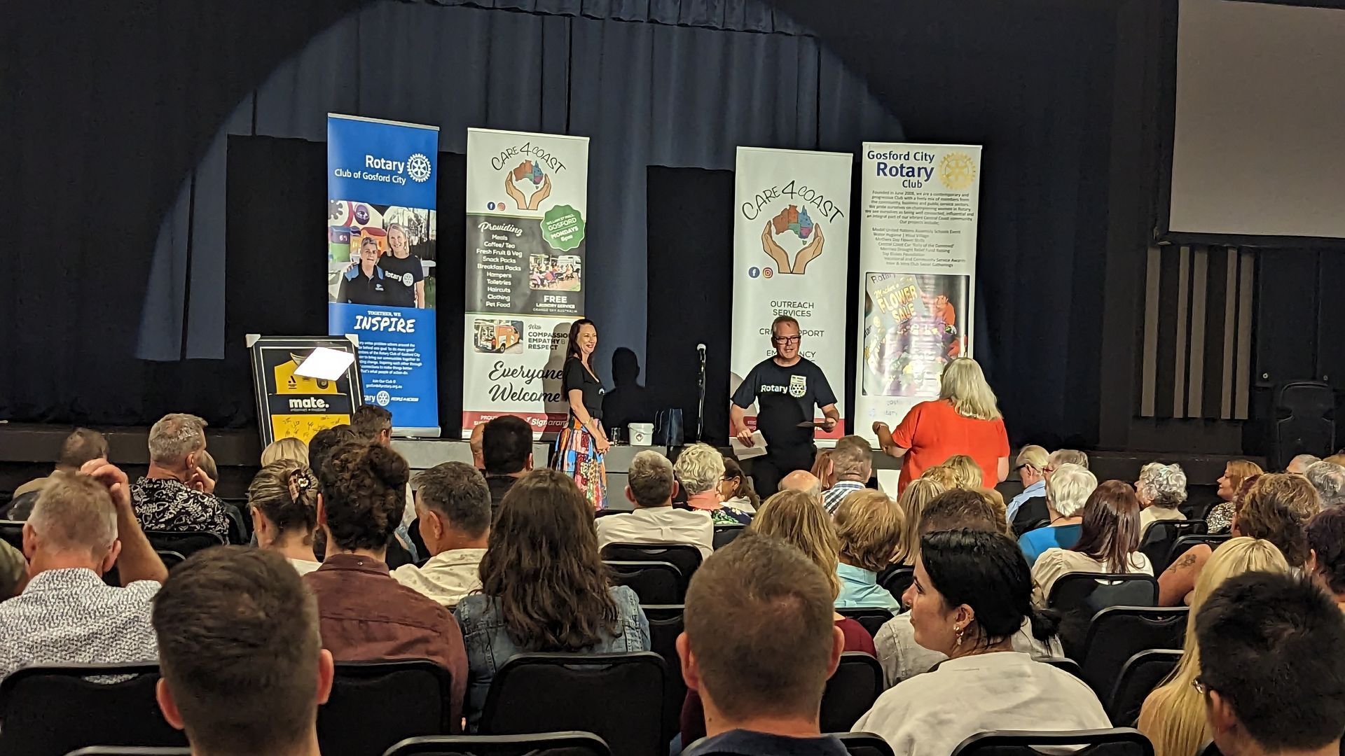 A large group of people are sitting in chairs in front of a stage.