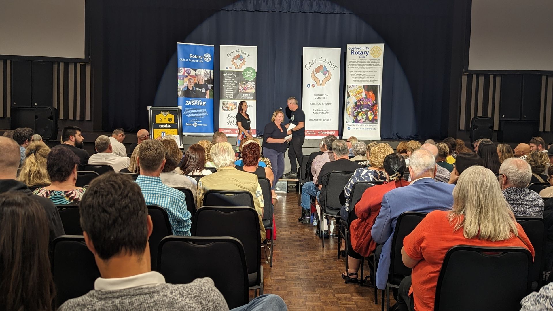 A large group of people are sitting in chairs in front of a stage.
