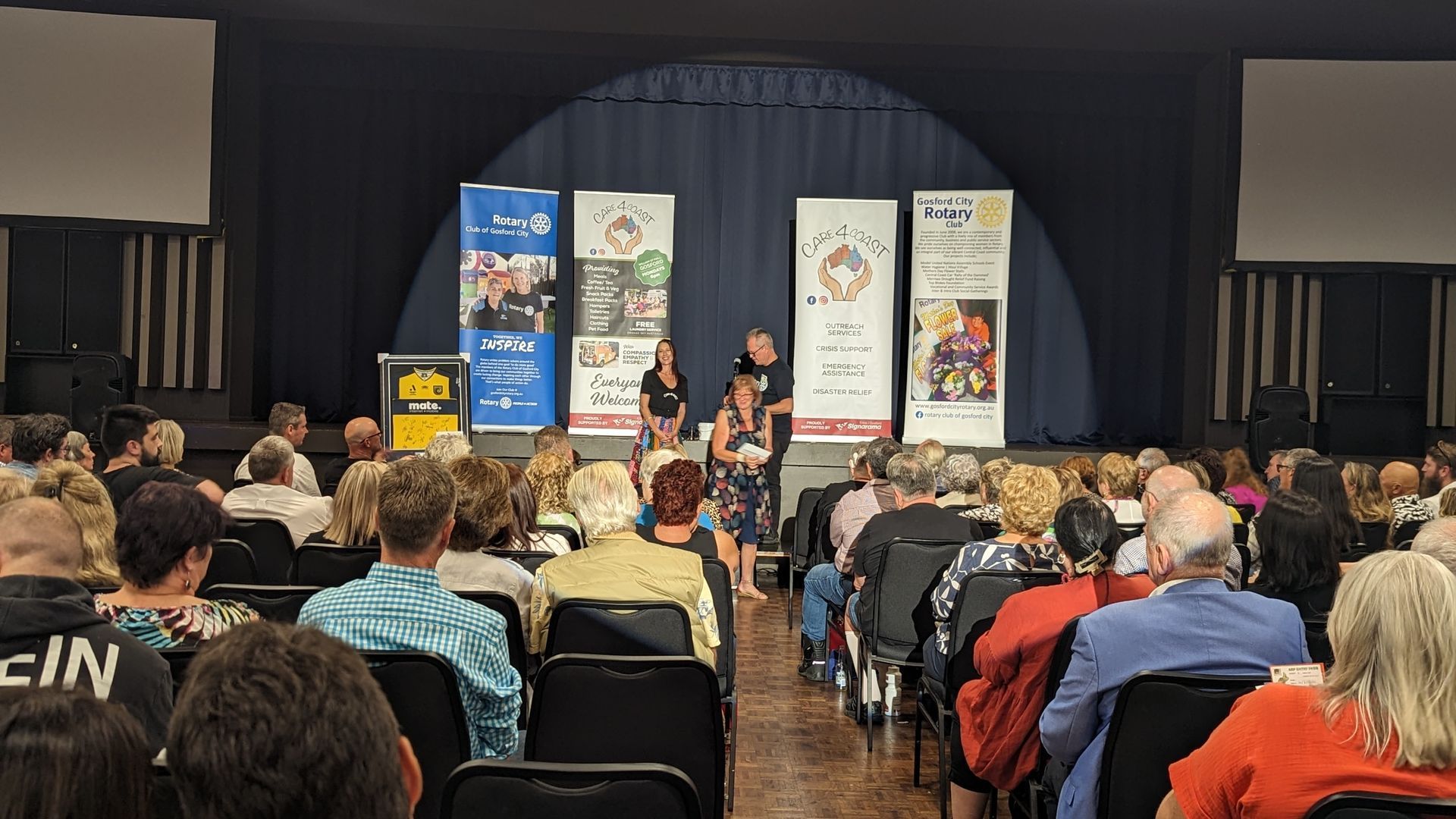 A large group of people are sitting in chairs in front of a stage.