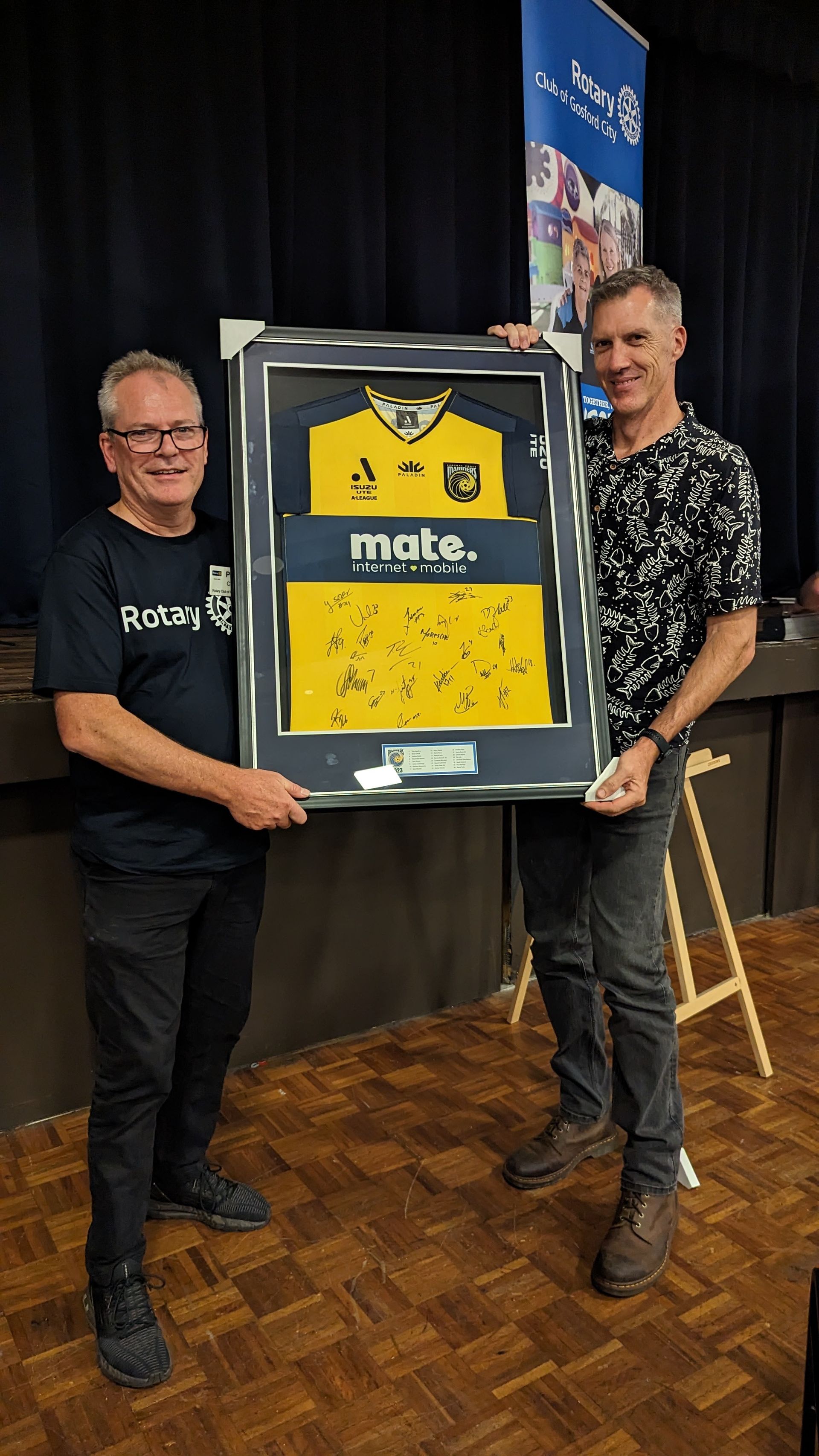 Two men are standing next to each other holding a framed jersey.
